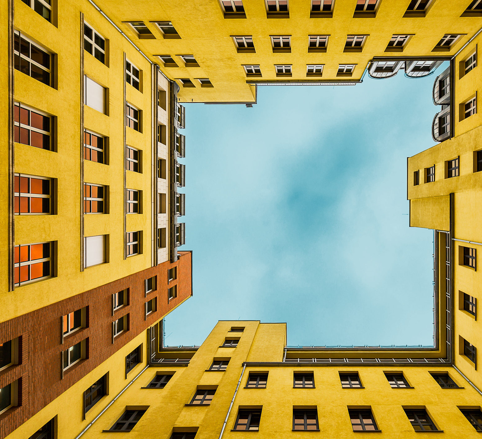 Symbolbild Supervision: Blick in den Himmel von einem Innenhof aus, um den ein hoher, gelber Wohnblock steht